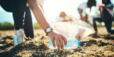 woman picking up empty water bottle from beach