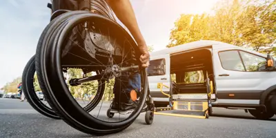 person in wheelchair approaching white van with accessible ramp