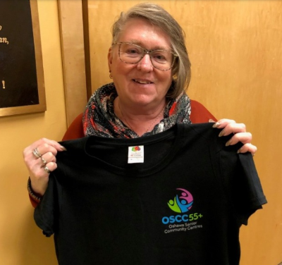 woman holding a black t-shirt with the OSCC55+ logo on it
