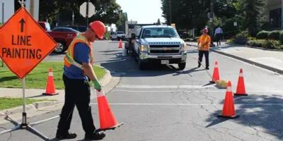 worker in hard hat and vest placing pilons on road