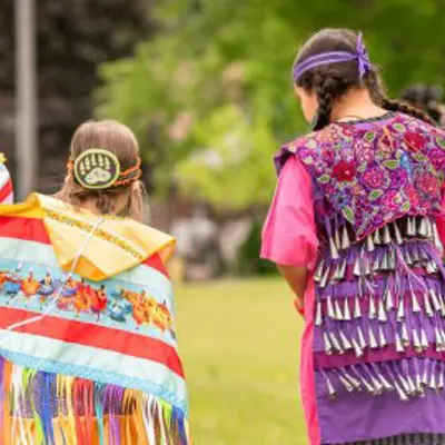 Two children walking away from the camera wearing regalia